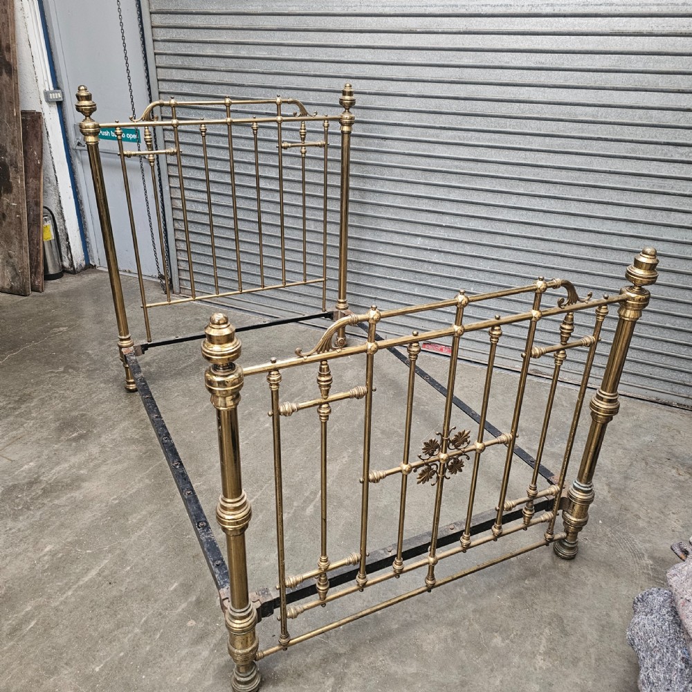 An antique Victorian double bed frame crafted with vertical brass spindles, decorative brass rosettes, turned urn finials, and a black cast iron base. View II