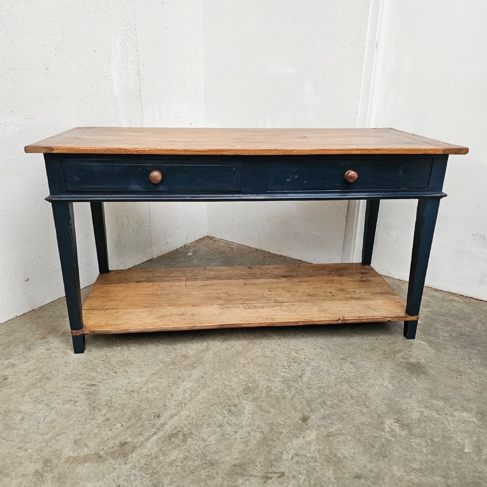 A French two-tier wooden work table featuring a dark blue painted frame, two drawers with round wooden handles, and natural light wood top and lower shelf.