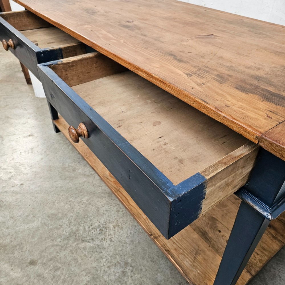 A French two-tier wooden work table featuring a dark blue painted frame, two drawers with round wooden handles, and natural light wood top and lower shelf. View VI