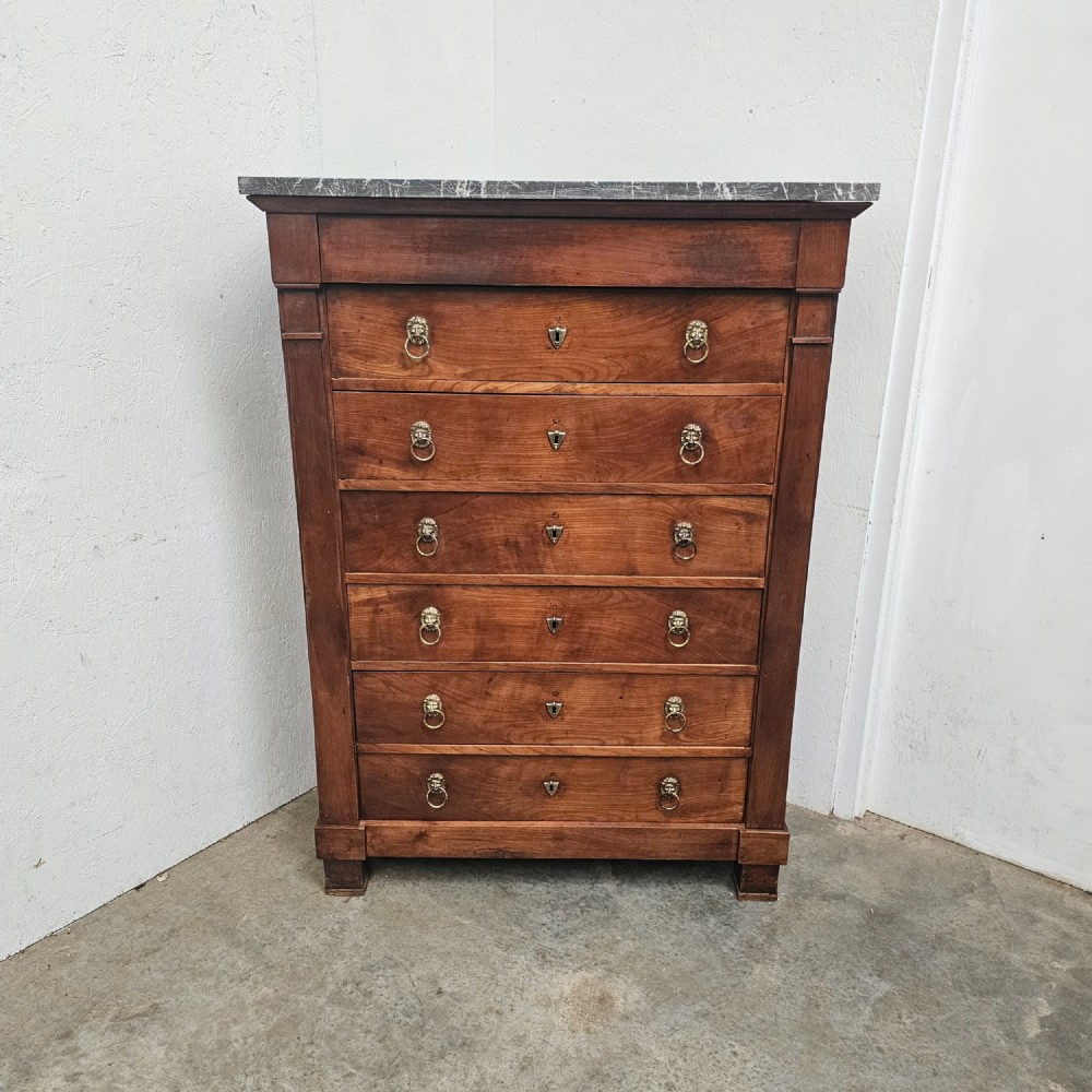 A nineteenth-century French cherry wood semainier featuring seven drawers with brass lion mask ring handles and a grey marble top.