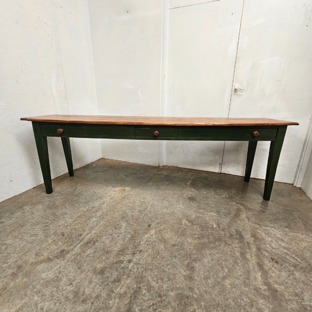 A long French painted pine console table featuring a natural wood plank top, a dark green painted base with tapered square legs, and three inline drawers with wooden knobs. View II