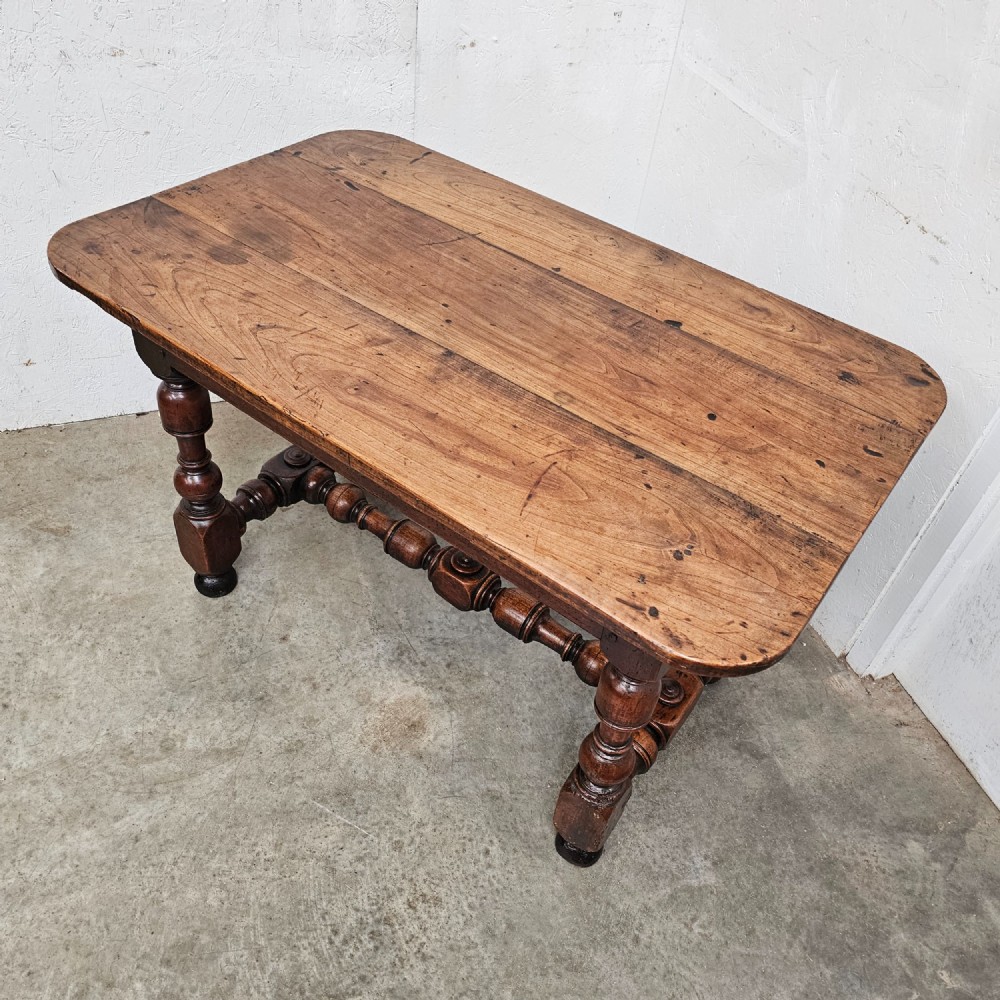 A warm brown cherry wood side table with turned legs, a low stretcher, and a single frieze drawer with a brass handle. View VI