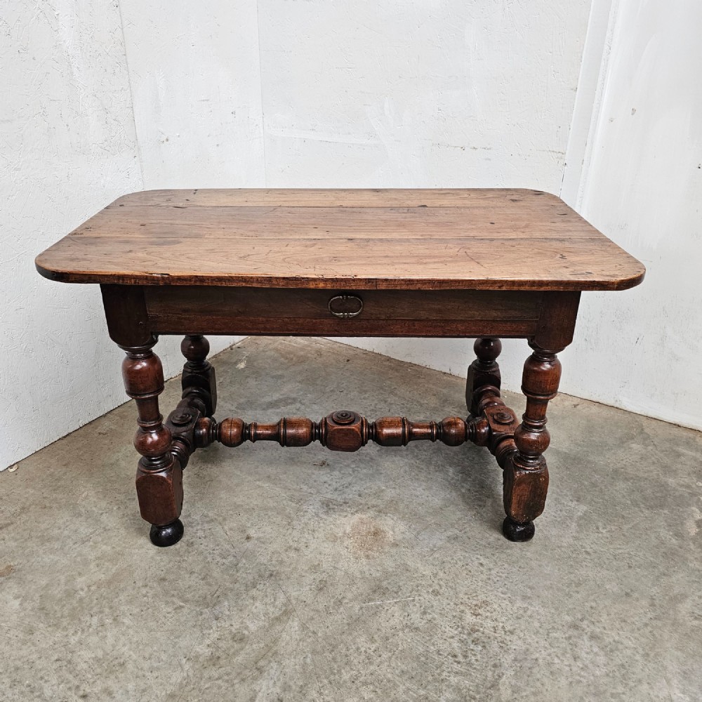 A warm brown cherry wood side table with turned legs, a low stretcher, and a single frieze drawer with a brass handle. View VII