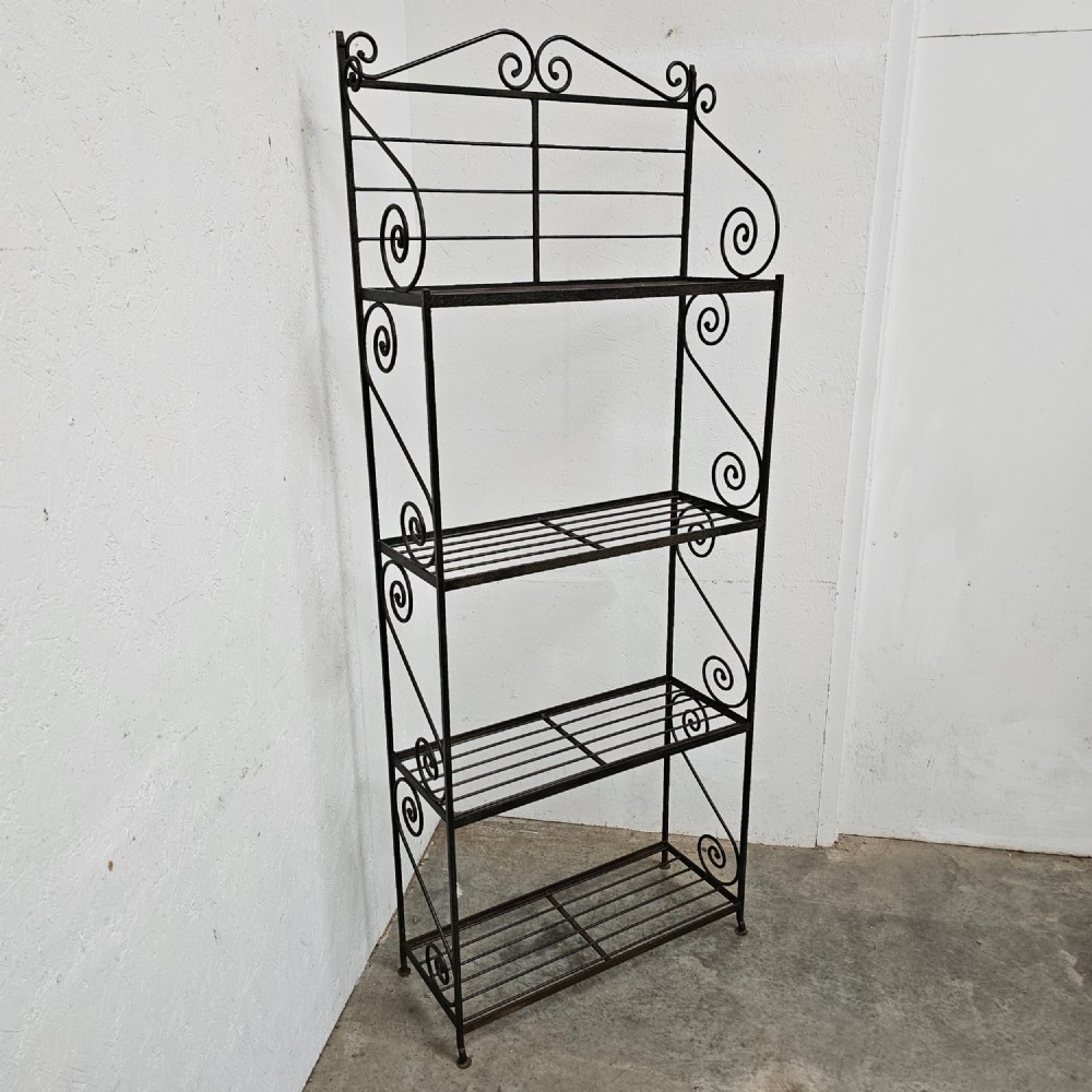A tall dark wrought iron bakers rack featuring four slatted open shelves, side lattice supports, and decorative scrollwork along the upper pediment. View IV