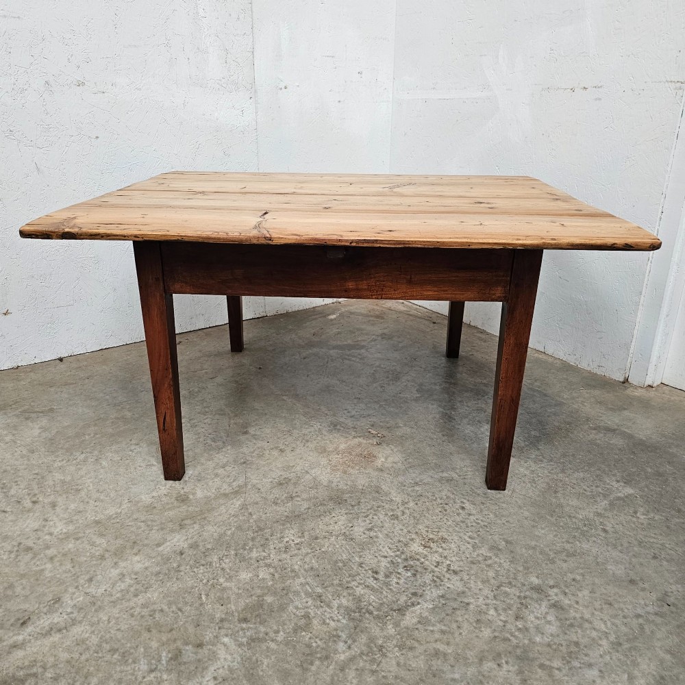 An antique table featuring an unvarnished scrubbed pine tabletop supported by a dark fruitwood base with square tapered legs.