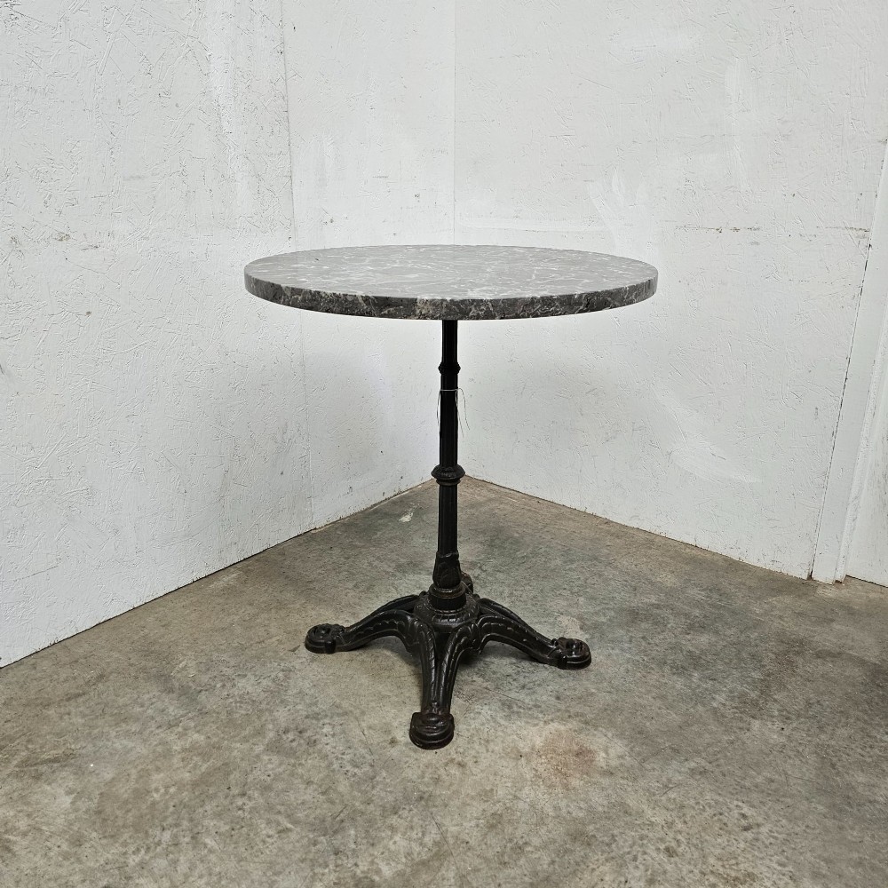 A French bistro table featuring a circular grey veined marble top resting on a dark cast iron pedestal base with decorative feet. View II