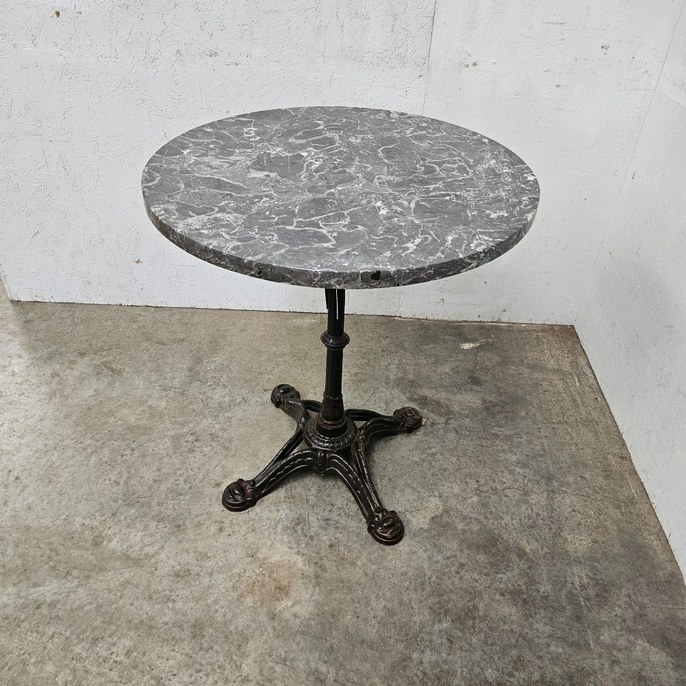 A French bistro table featuring a circular grey veined marble top resting on a dark cast iron pedestal base with decorative feet. View III
