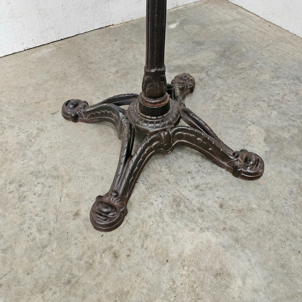 A French bistro table featuring a circular grey veined marble top resting on a dark cast iron pedestal base with decorative feet. View IV