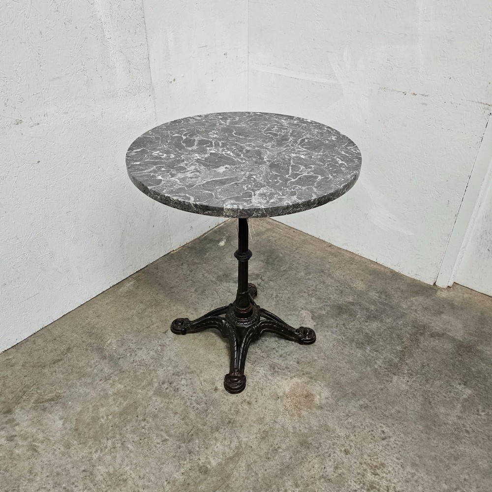 A French bistro table featuring a circular grey veined marble top resting on a dark cast iron pedestal base with decorative feet. View V