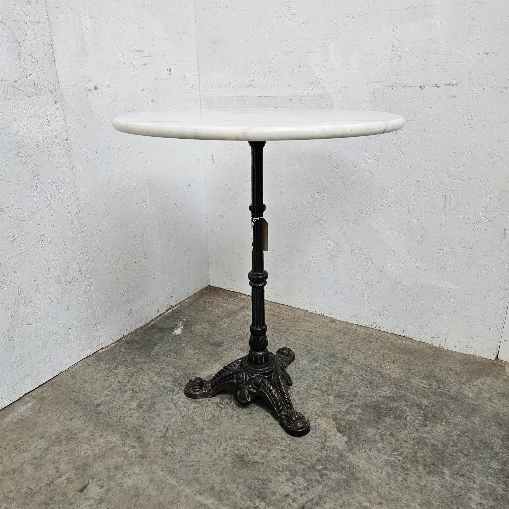 A round white marble top bistro table supported by a black cast iron central column and ornate tripod base.