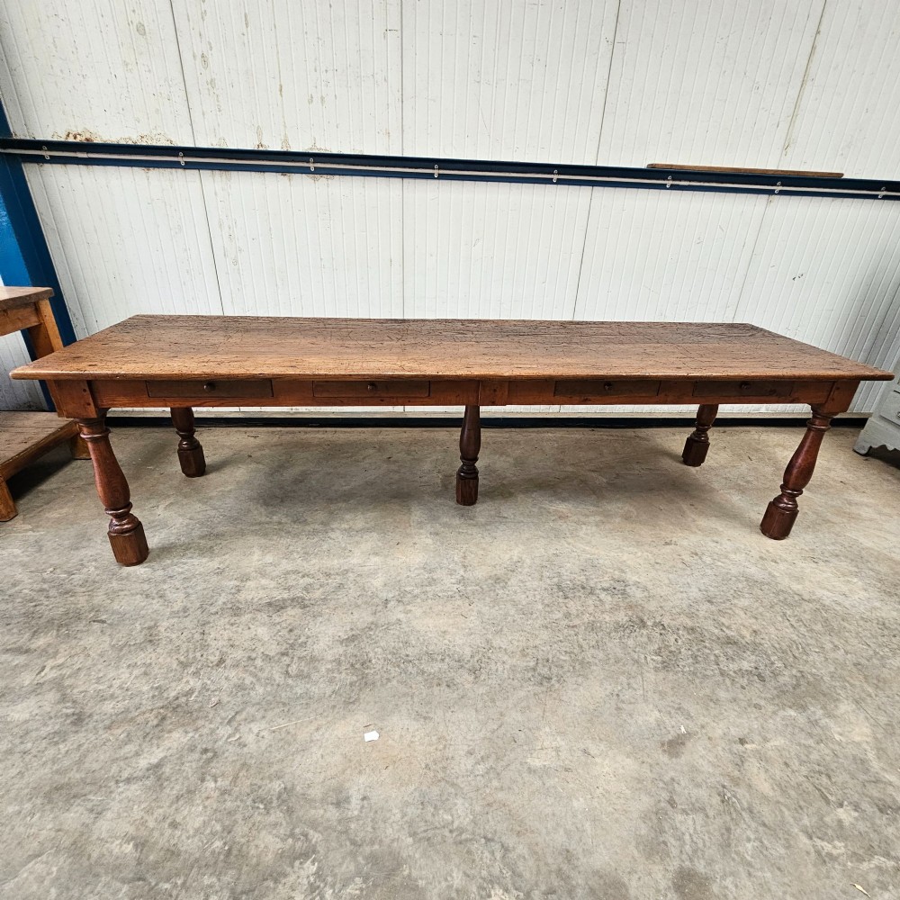 A long rustic chestnut and pine farmhouse dining table featuring six turned legs and multiple side drawers along the wooden frame. View IV