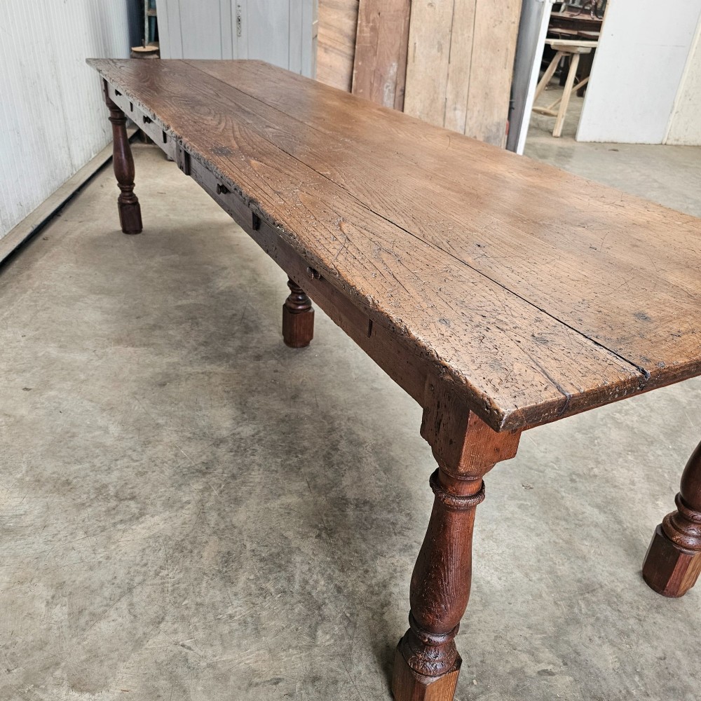 A long rustic chestnut and pine farmhouse dining table featuring six turned legs and multiple side drawers along the wooden frame. View V