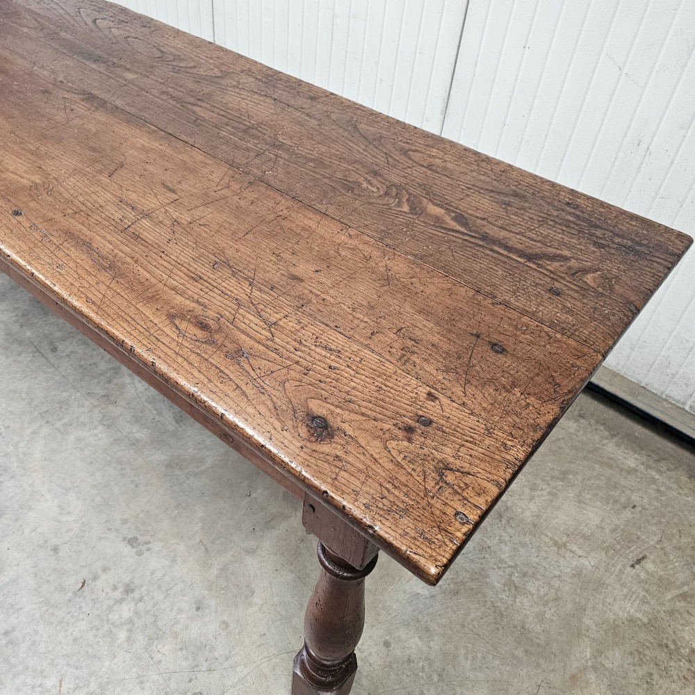 A long rustic chestnut and pine farmhouse dining table featuring six turned legs and multiple side drawers along the wooden frame. View VI