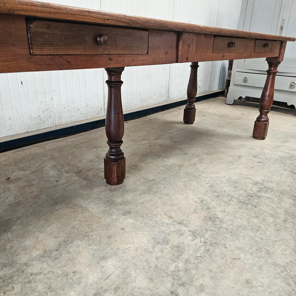 A long rustic chestnut and pine farmhouse dining table featuring six turned legs and multiple side drawers along the wooden frame. View VII