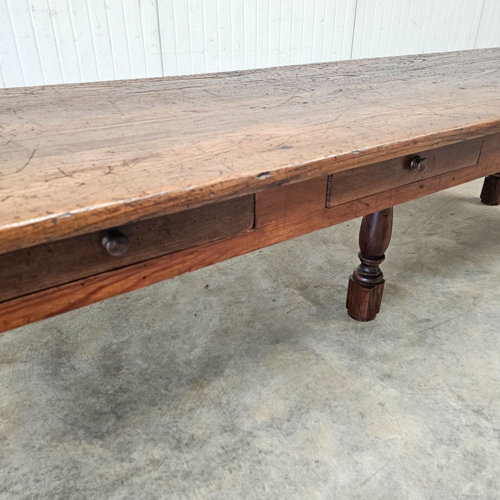 A long rustic chestnut and pine farmhouse dining table featuring six turned legs and multiple side drawers along the wooden frame. View VIII