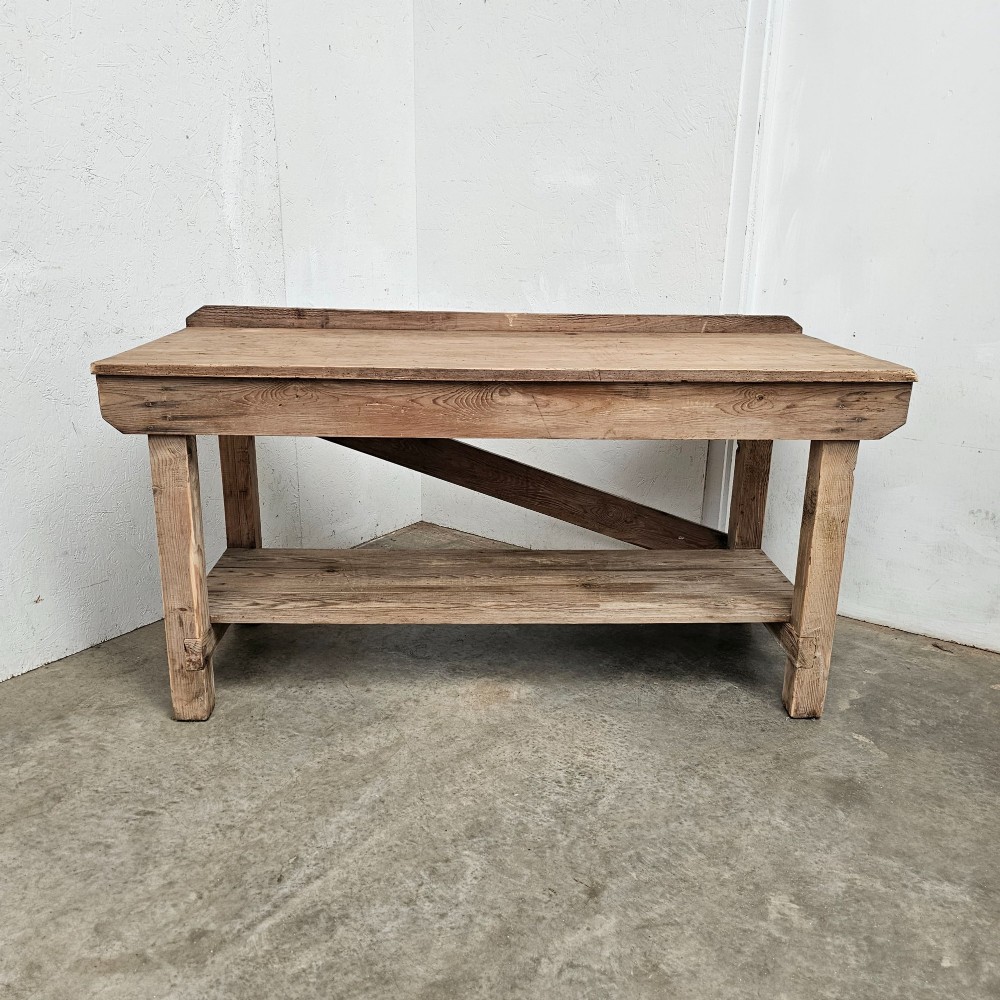 A rustic pine potting table featuring a raised rear upstand, sturdy square legs with a diagonal crossbrace, and a full-length lower timber shelf.