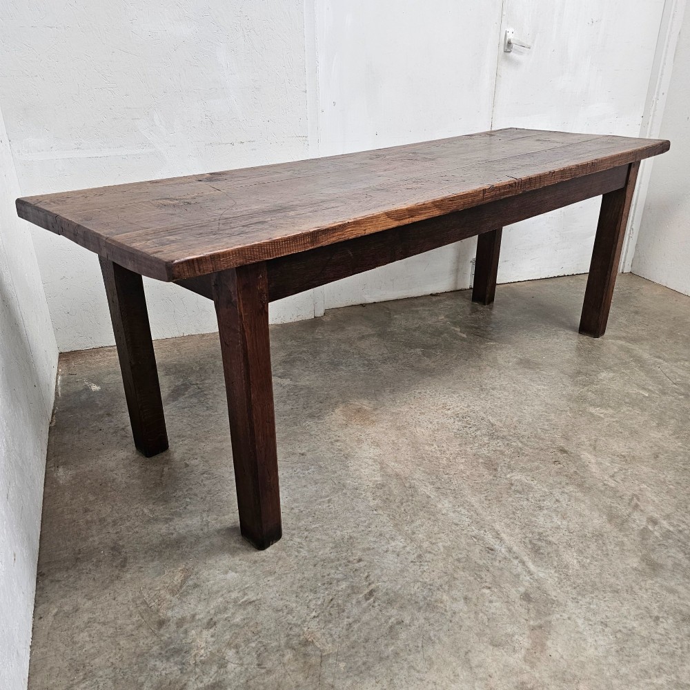 A long antique dark oak tavern table featuring a thick planked timber top supported by sturdy square legs.