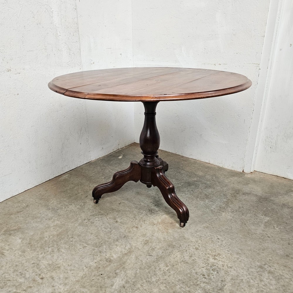 A round antique timber table supported by a central turned pedestal column ending in three carved legs on castors.