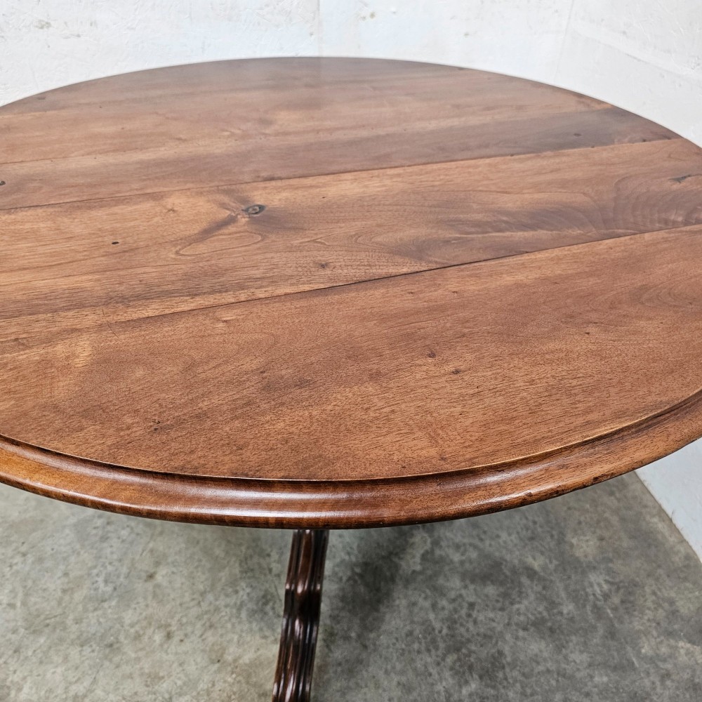 A round antique timber table supported by a central turned pedestal column ending in three carved legs on castors. View II