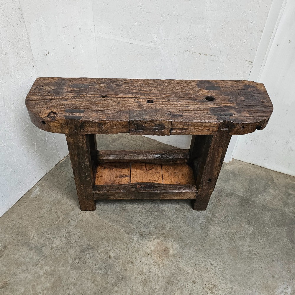 A small primitive French elm workbench featuring a thick distressed wood top, heavy trestle legs, and a lower storage shelf. View IV