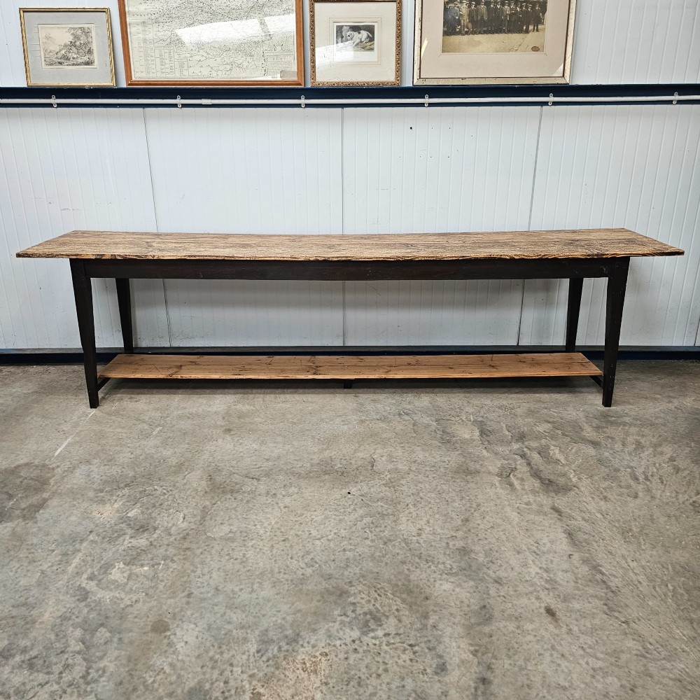 A long two-tier timber harvest table with a natural pine plank top and a dark brown frame featuring a full-length lower shelf.