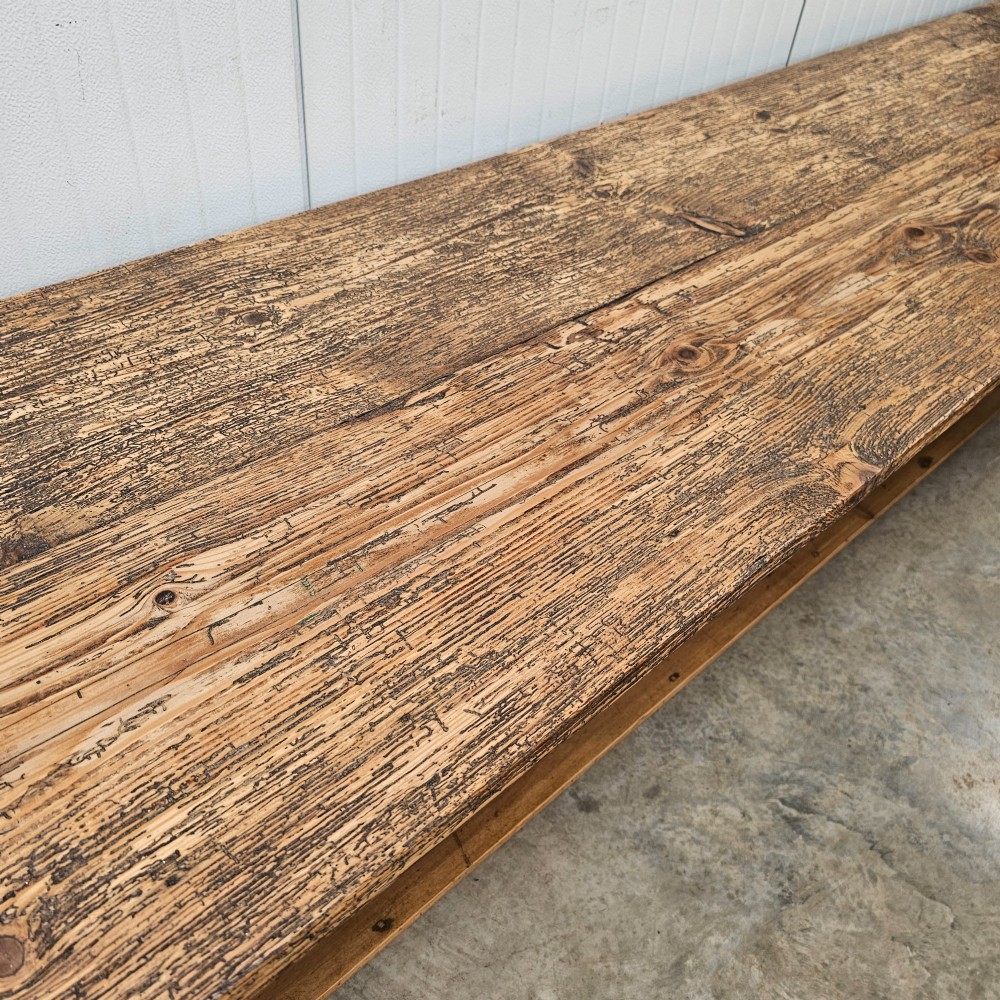 A long two-tier timber harvest table with a natural pine plank top and a dark brown frame featuring a full-length lower shelf. View III