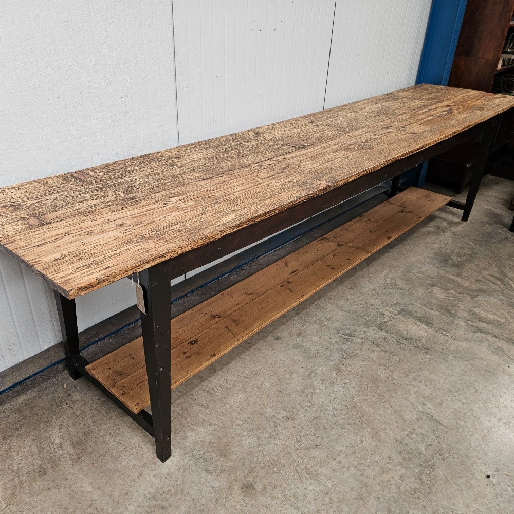 A long two-tier timber harvest table with a natural pine plank top and a dark brown frame featuring a full-length lower shelf. View IV