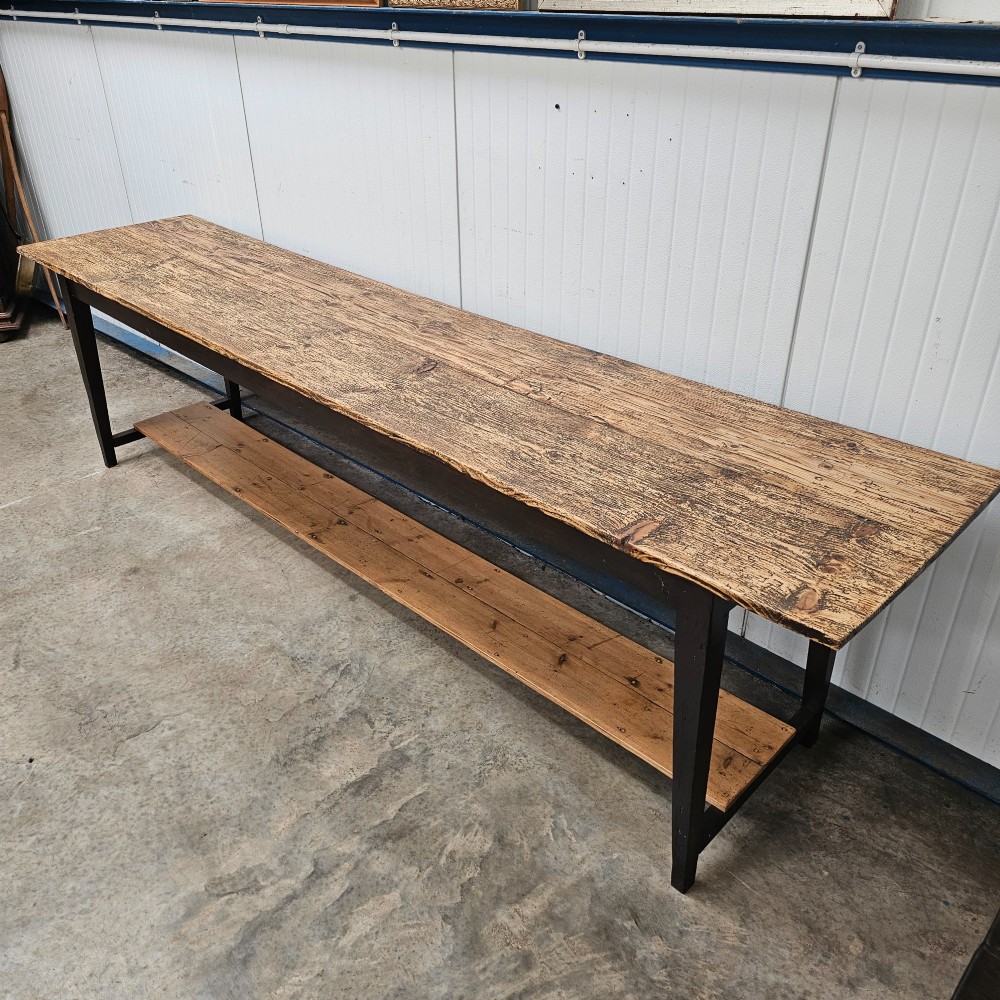 A long two-tier timber harvest table with a natural pine plank top and a dark brown frame featuring a full-length lower shelf. View II