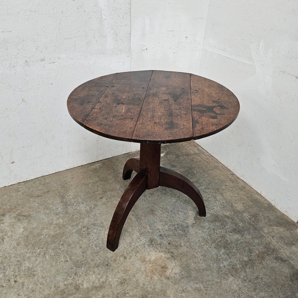 A dark oak round tilt-top table shown tilted vertically, supported by a central column and three curved tripod legs. View II
