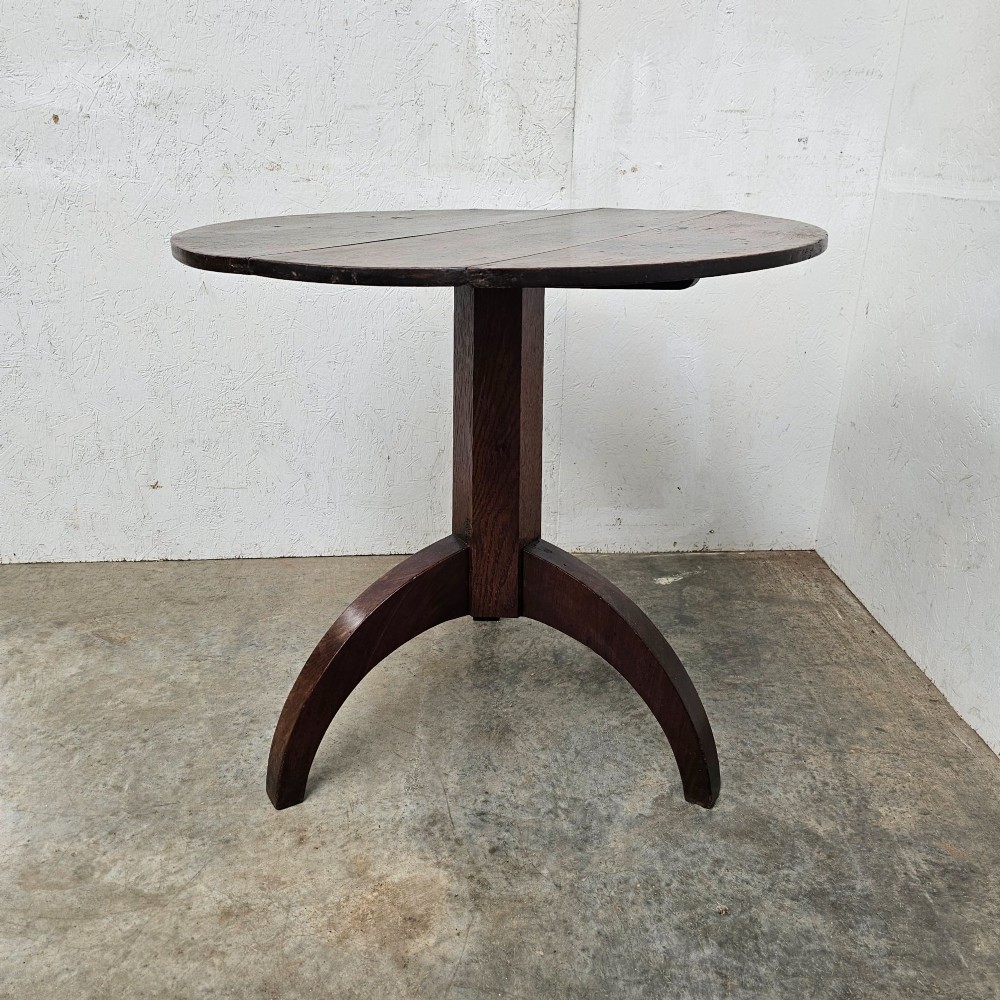 A dark oak round tilt-top table shown tilted vertically, supported by a central column and three curved tripod legs. View III