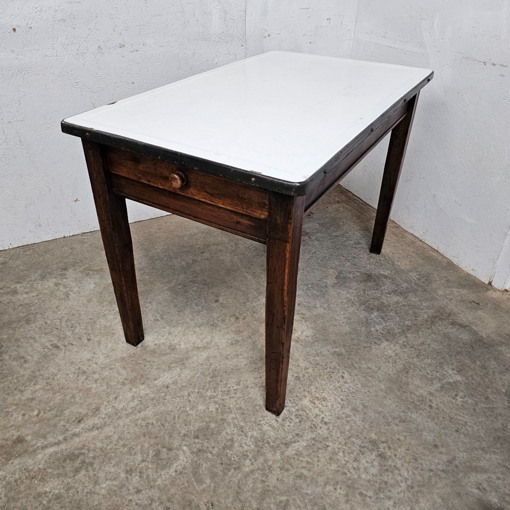 An early 20th-century dark oak kitchen prep table featuring a white vitreous enamel top and a single frieze drawer with a wooden knob.