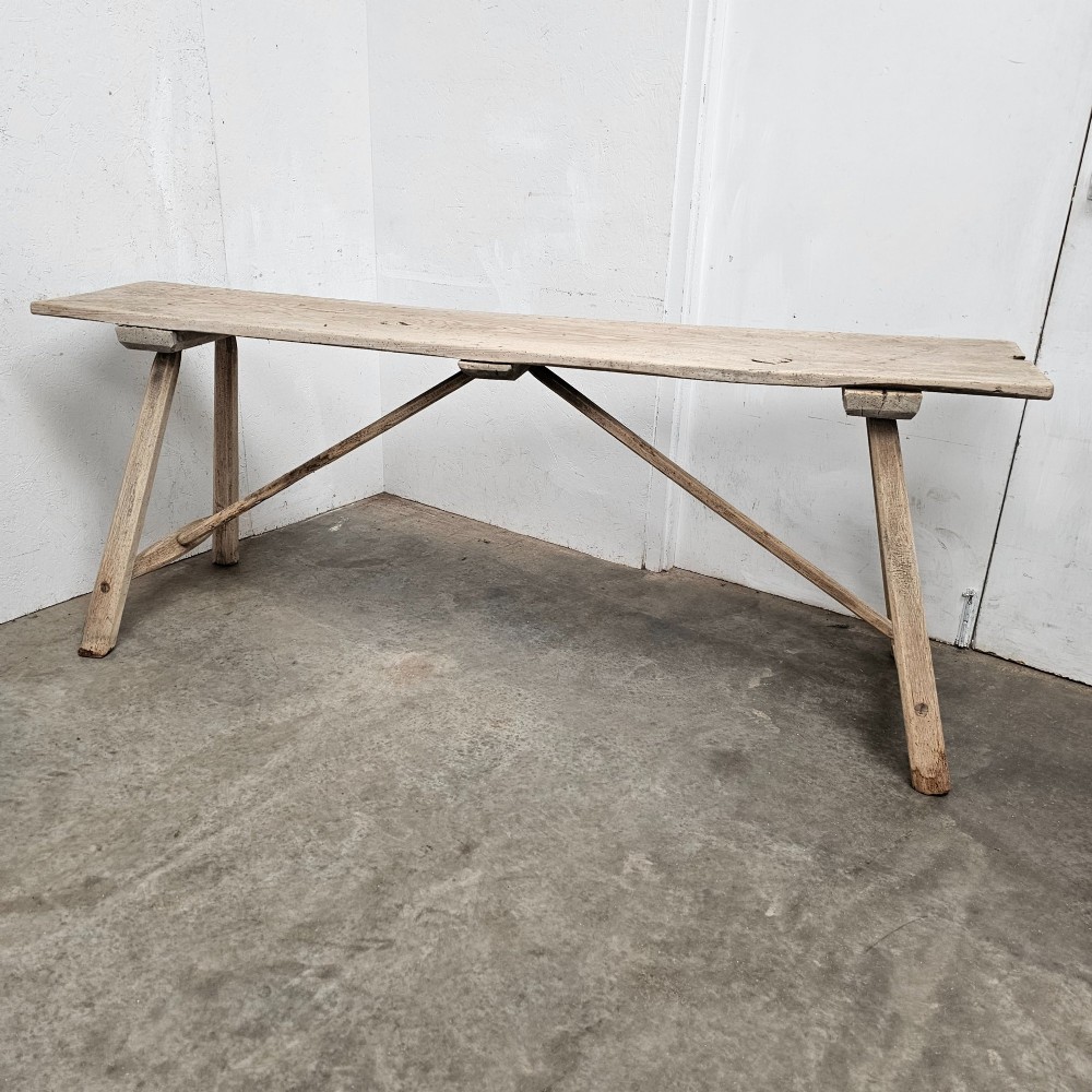 A long, narrow antique scrubbed pine console table featuring angled legs with diagonal cross-bracing and an unvarnished timber finish.