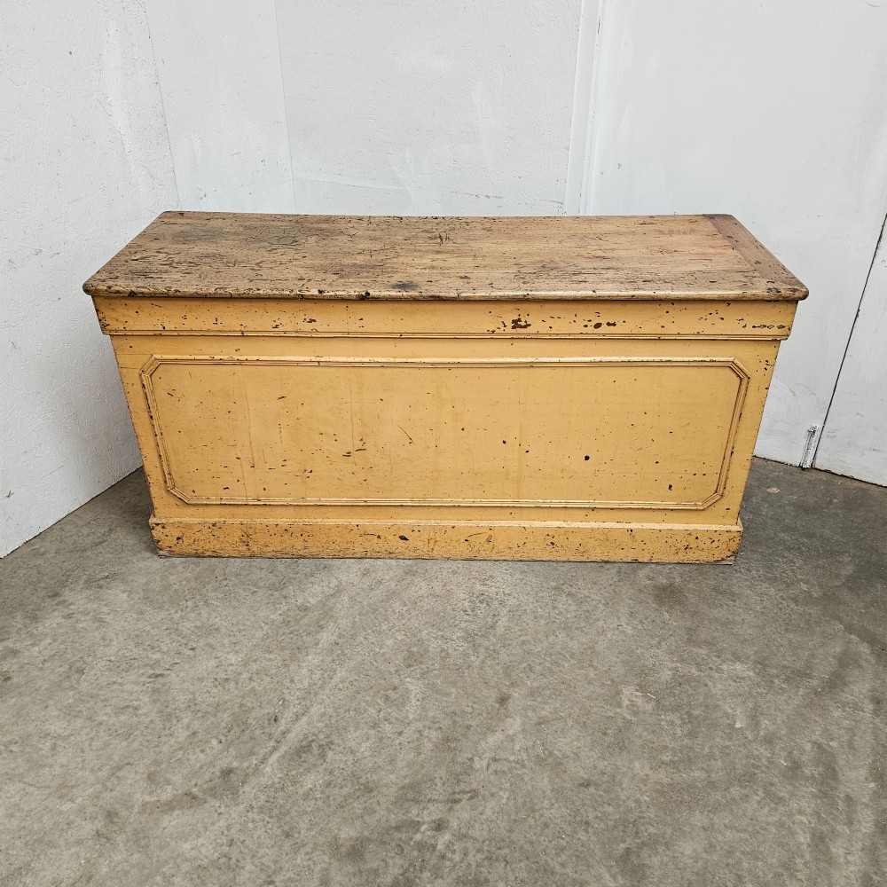 A large rectangular timber shop counter featuring a distressed yellow painted frame with a moulded front panel and a natural wood top. View III