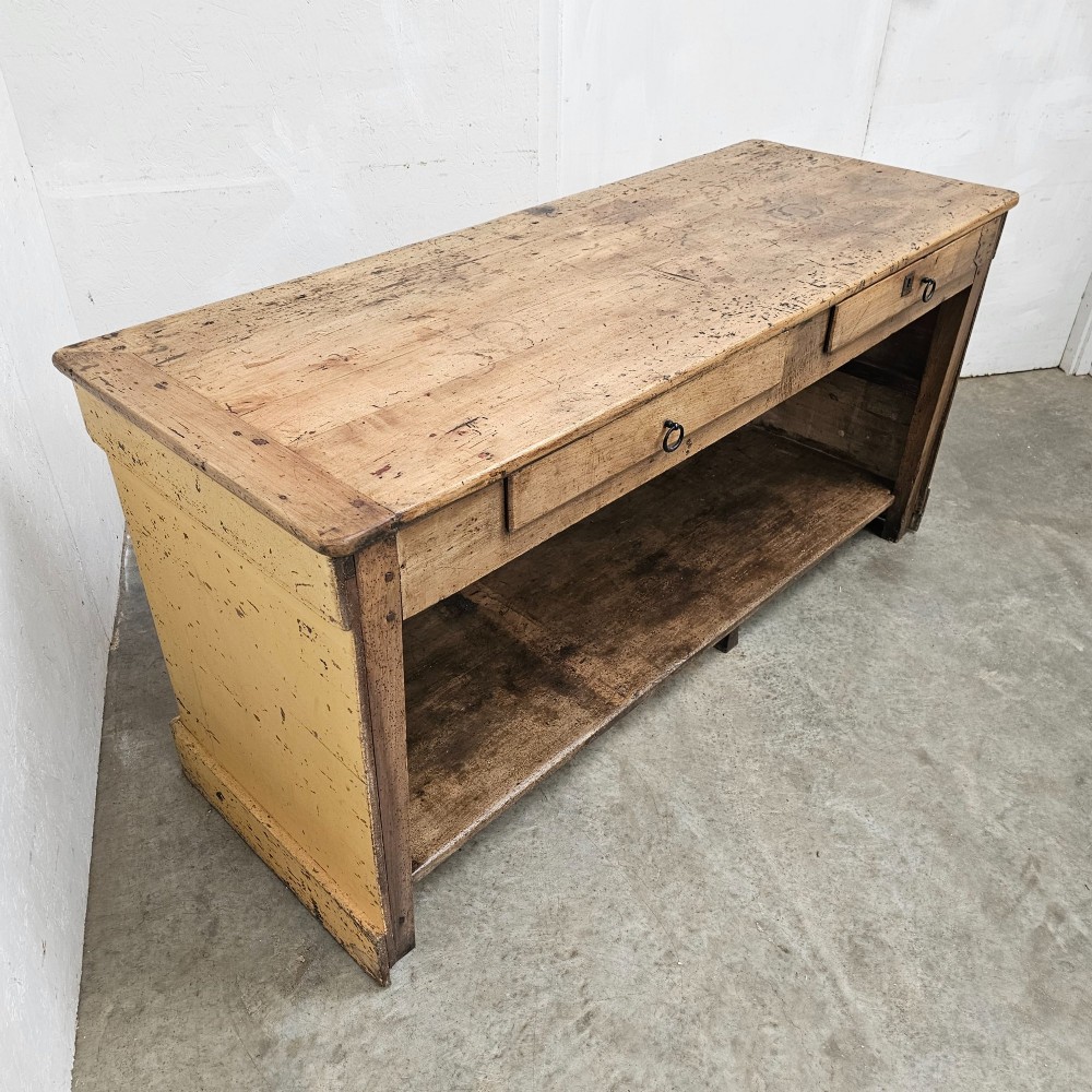 A large rectangular timber shop counter featuring a distressed yellow painted frame with a moulded front panel and a natural wood top. View V