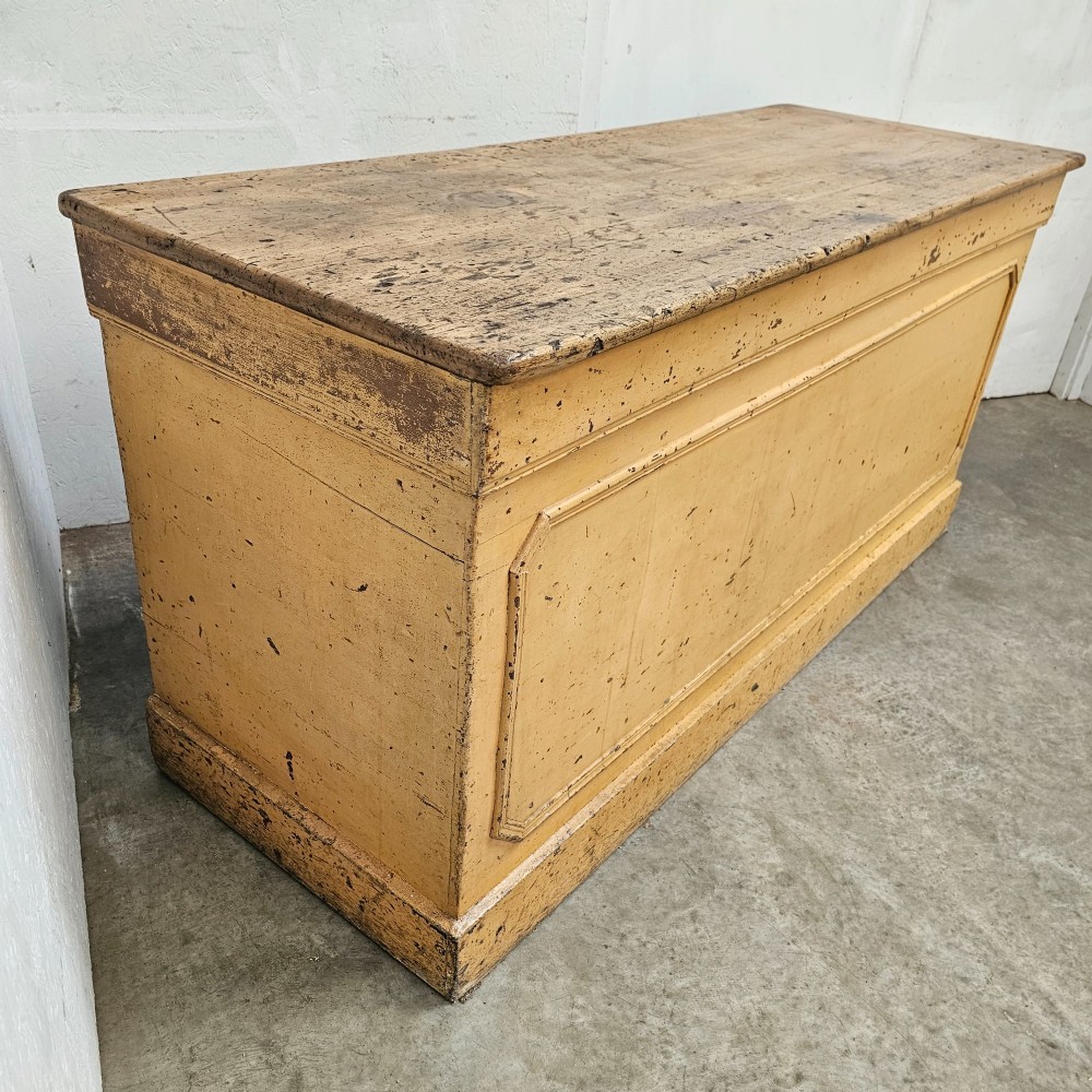 A large rectangular timber shop counter featuring a distressed yellow painted frame with a moulded front panel and a natural wood top. View VIII