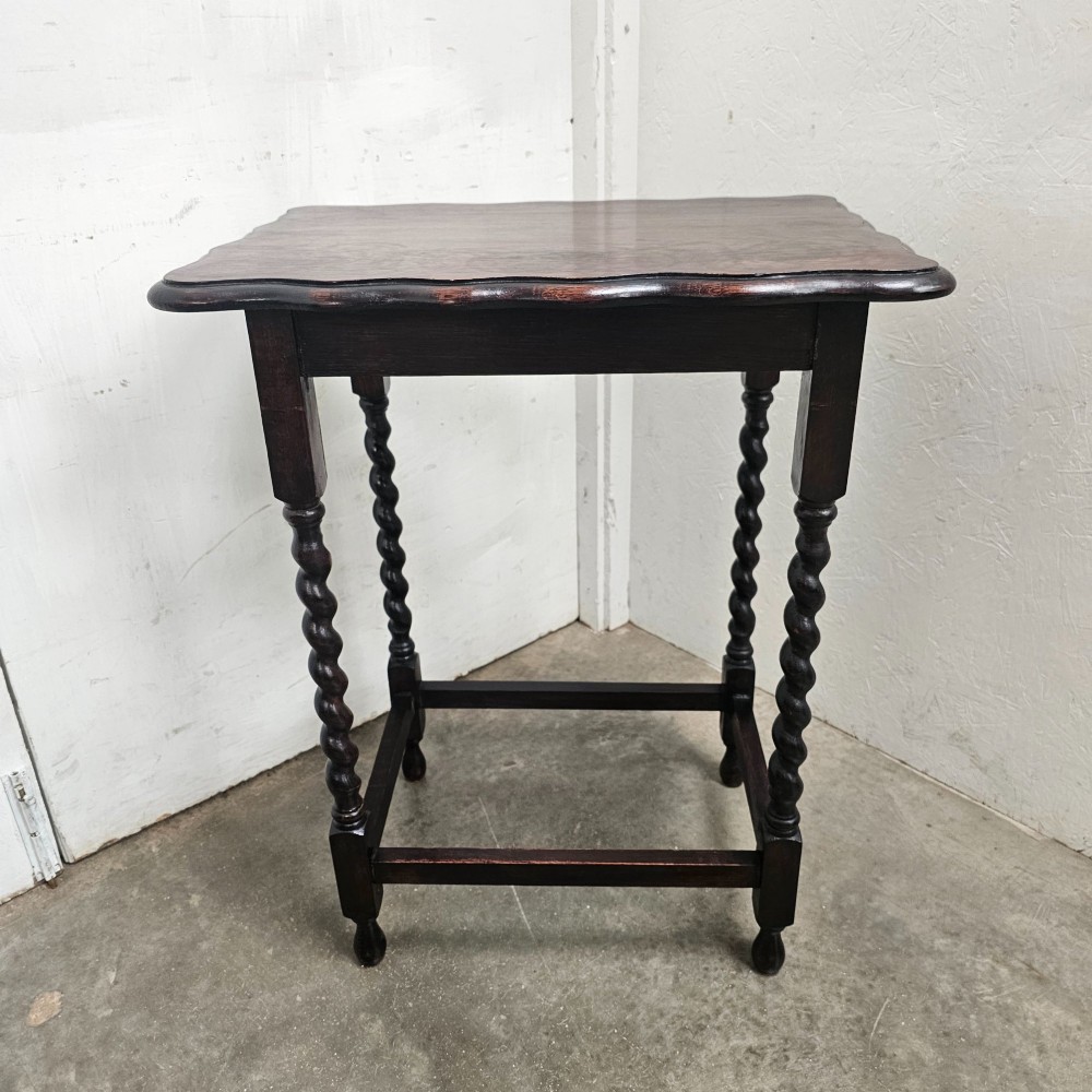 A dark oak side table with a scalloped pie-crust top, four barley-twist turned legs, and a square base stretcher.