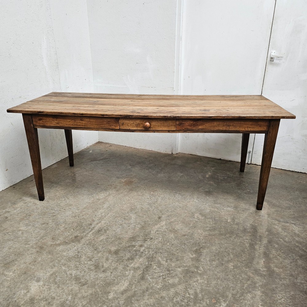 An antique French farmhouse dining table crafted with a planked pine top, oak apron, single frieze drawer with a turned wooden knob, and tapered square legs.