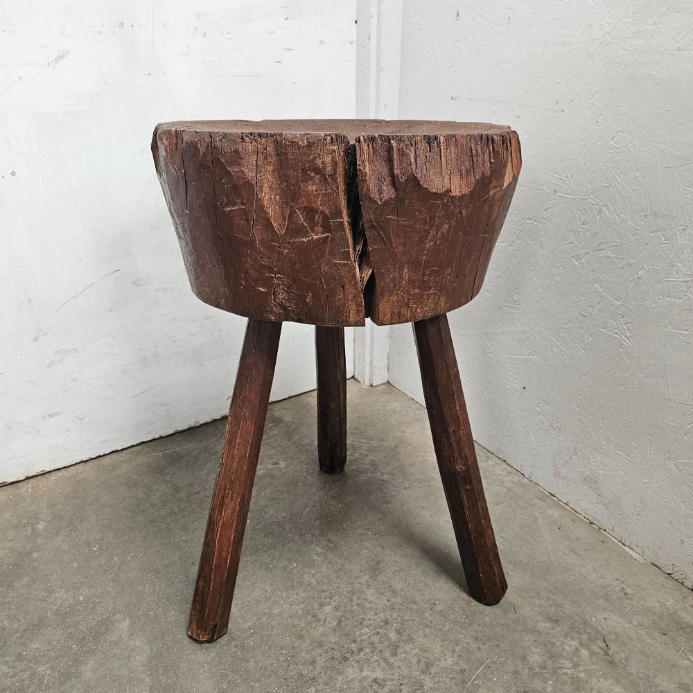 A primitive French beech game block with a carved timber top supported by three splayed wooden legs.