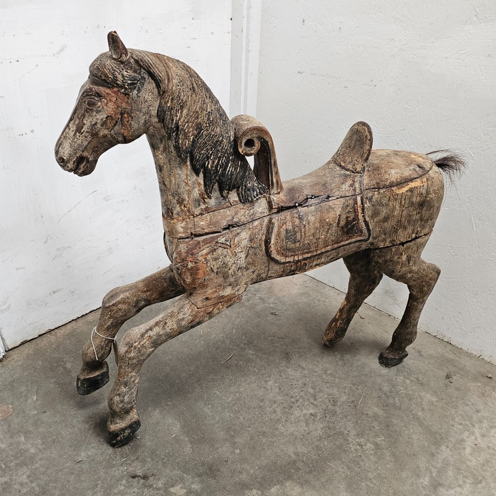 A 19th-century French hand-carved wooden carousel horse featuring a prancing pose, carved saddle, black painted mane, and weathered grey-brown timber finish.