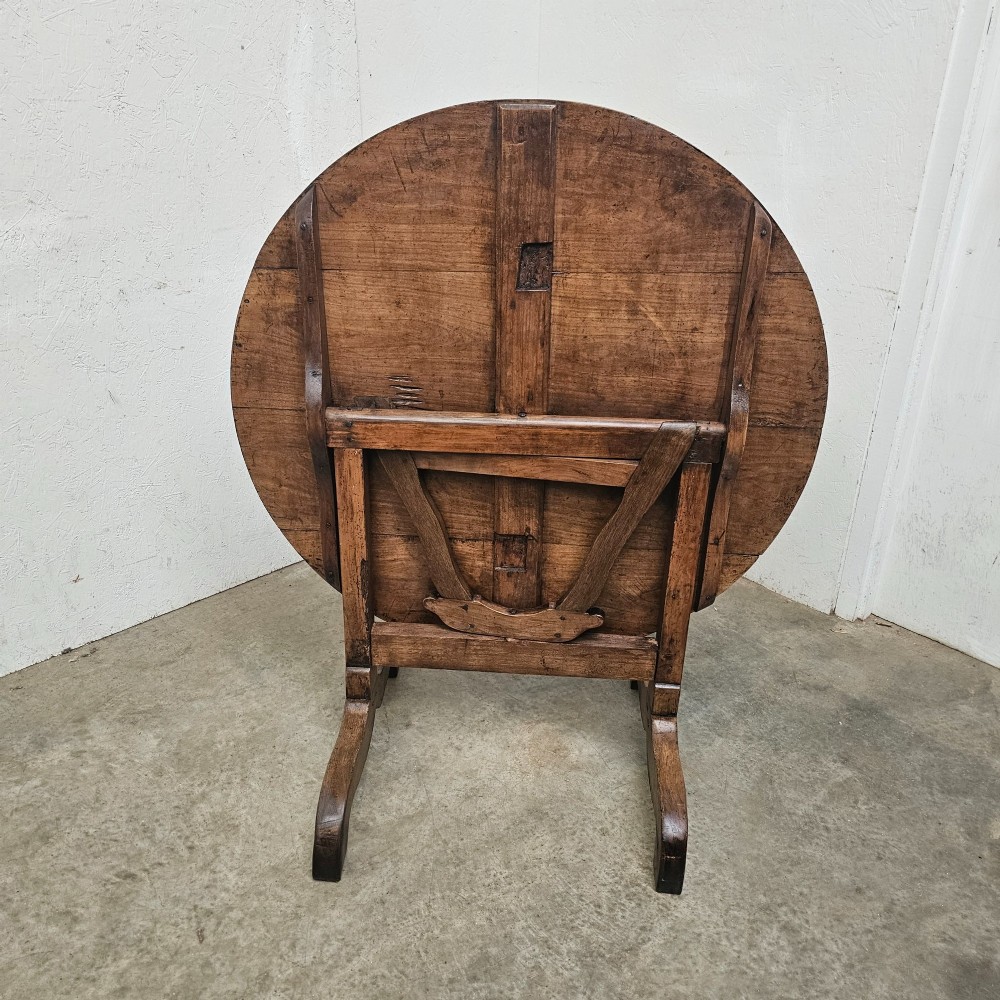 A circular French provincial folding vendange table crafted from oak and cherrywood with a planked surface tilted vertically on a trestle base. View II