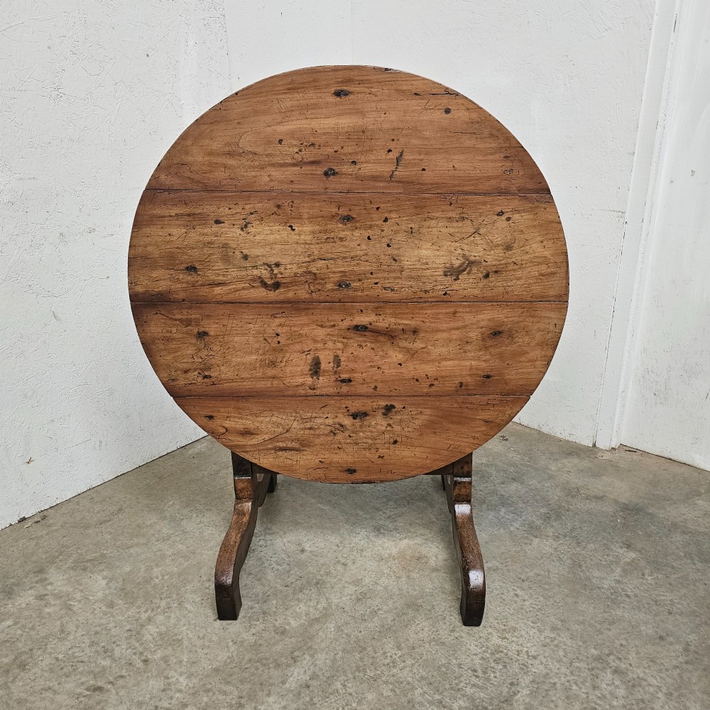 A circular French provincial folding vendange table crafted from oak and cherrywood with a planked surface tilted vertically on a trestle base.