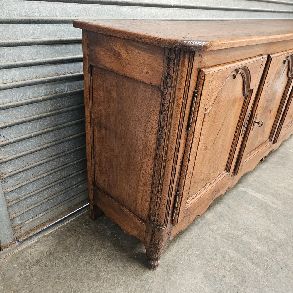 An 18th-century French provincial walnut four-door sideboard featuring hand-carved arched door panels, dark metal escutcheons, and a scalloped lower apron. View II