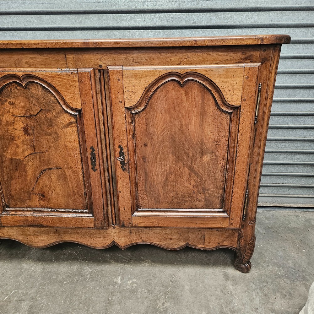 An 18th-century French provincial walnut four-door sideboard featuring hand-carved arched door panels, dark metal escutcheons, and a scalloped lower apron. View IV