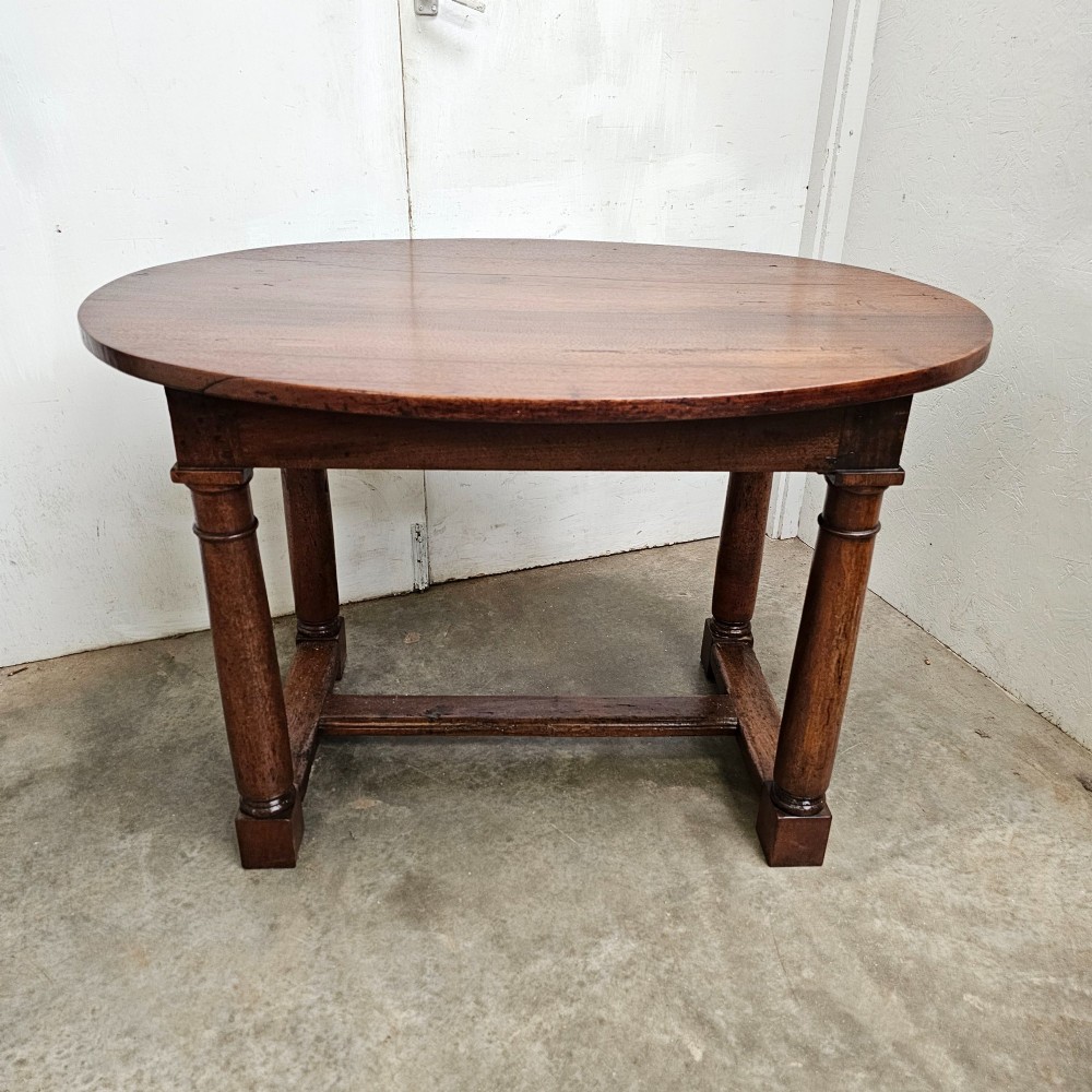 An 18th-century French oval walnut table featuring four turned legs joined by a low H-stretcher.