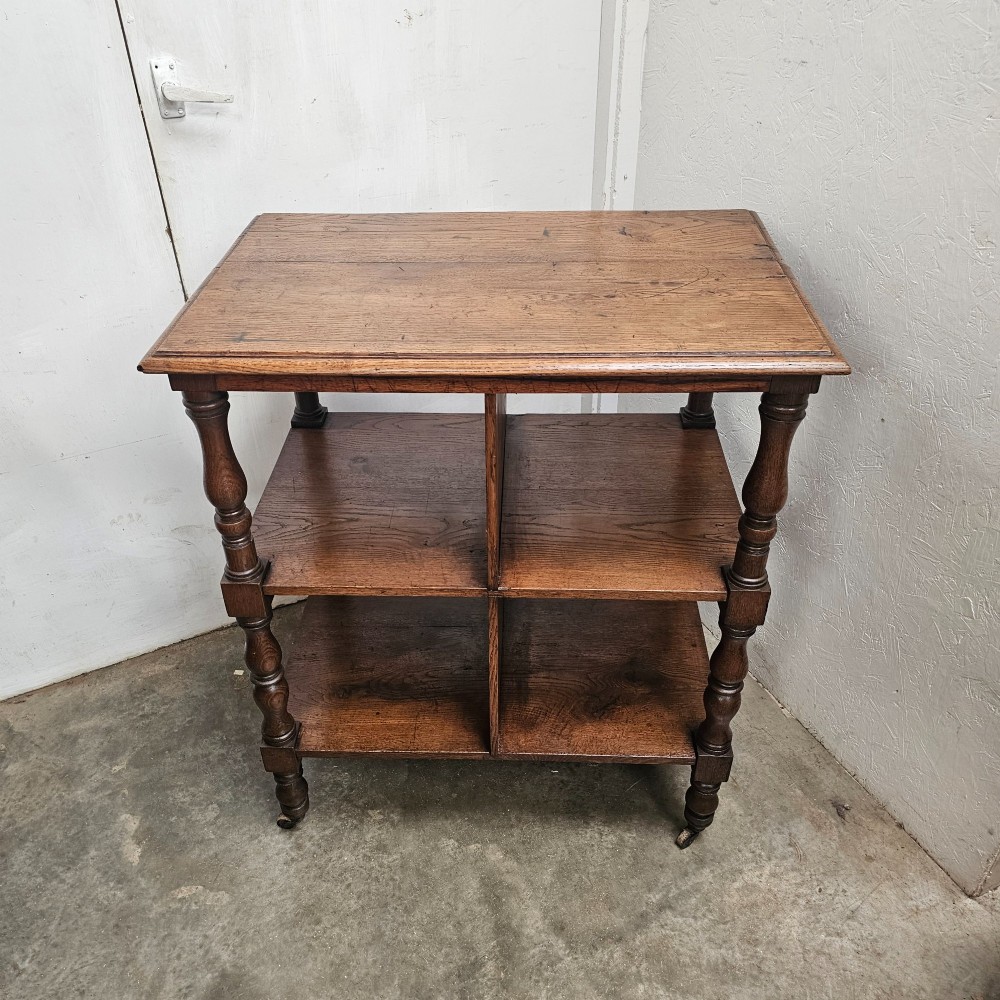 A dark oak library cart featuring three tiered shelves, central partitions, turned legs, and small metal castors. View IV