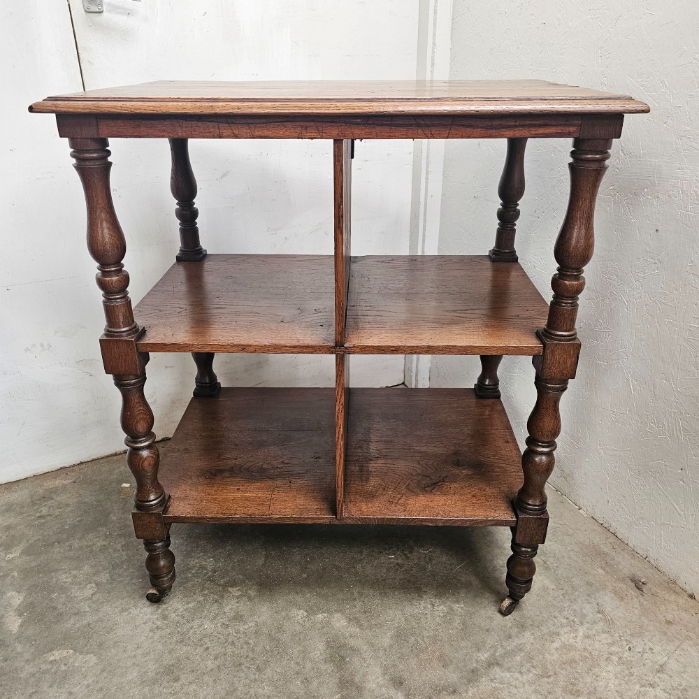 A dark oak library cart featuring three tiered shelves, central partitions, turned legs, and small metal castors. View V