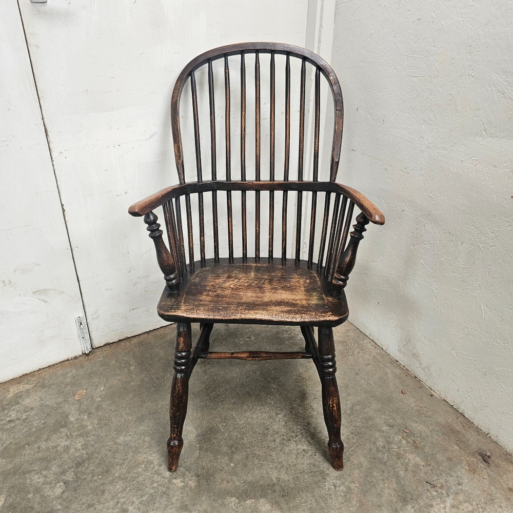 An antique dark brown oak and ash Windsor armchair featuring a high hoop back with vertical spindles, turned legs, and a shaped solid wood seat.