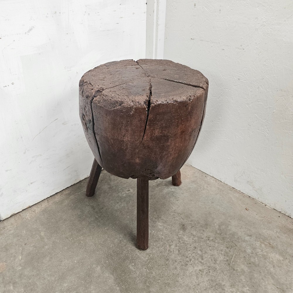A solid dark brown carved beech timber game block mounted on three splayed wooden legs with natural surface splits.