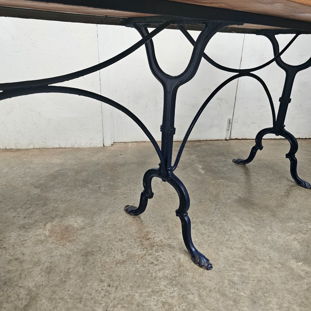 A long rectangular light elm wood table top supported by three curved black iron legs with arching stretchers. View II