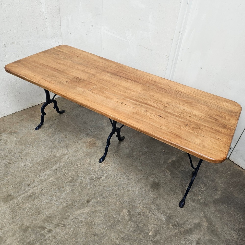 A long rectangular light elm wood table top supported by three curved black iron legs with arching stretchers. View IV